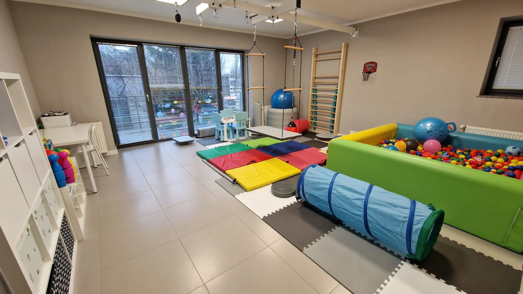 Sala z basenem z piłkami, tunelem i kolorowymi materacami przy przeszklonej ścianie