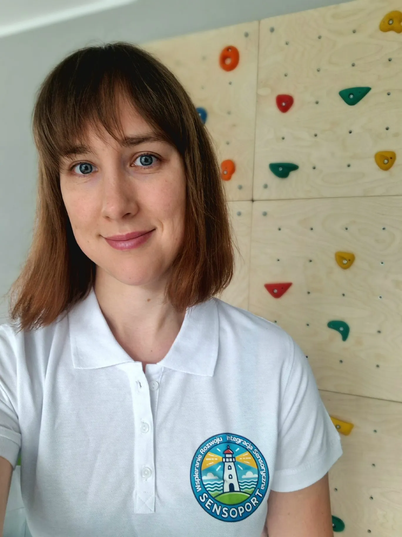Ewelina Aluk w koszulce z logo SensoPortu, na tle ścianki wspinaczkowej