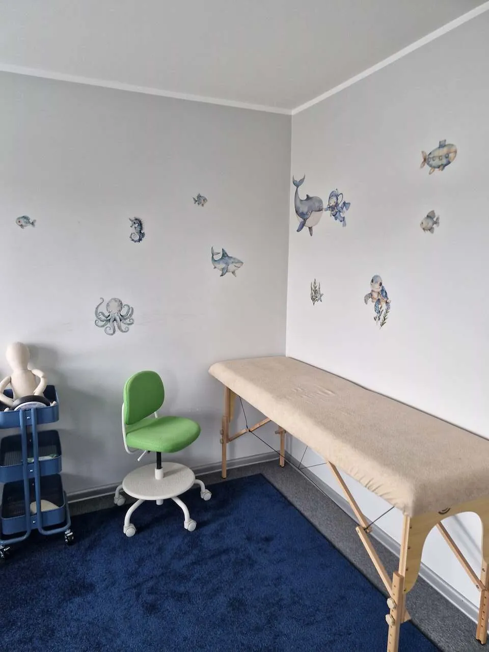 Gabinet z leżanką terapeutyczną, zielonym krzesełkiem dla dziecka i naklejkami z morskimi zwierzętami na ścianach