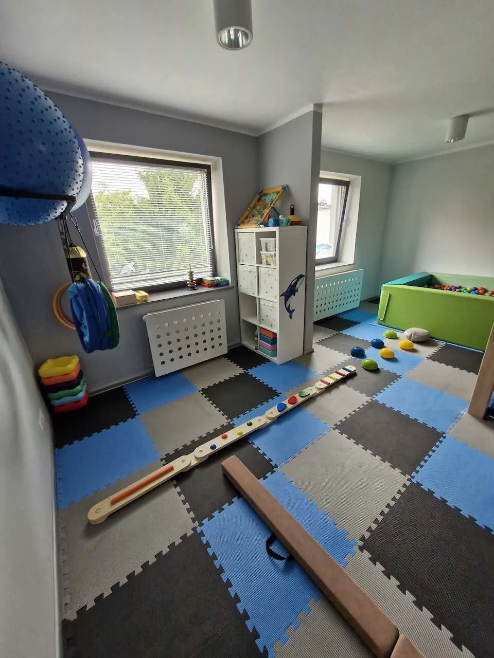 Sala z drewnianą ścieżką równoważną, kolorowymi dyskami sensorycznymi i basenem z piłkami