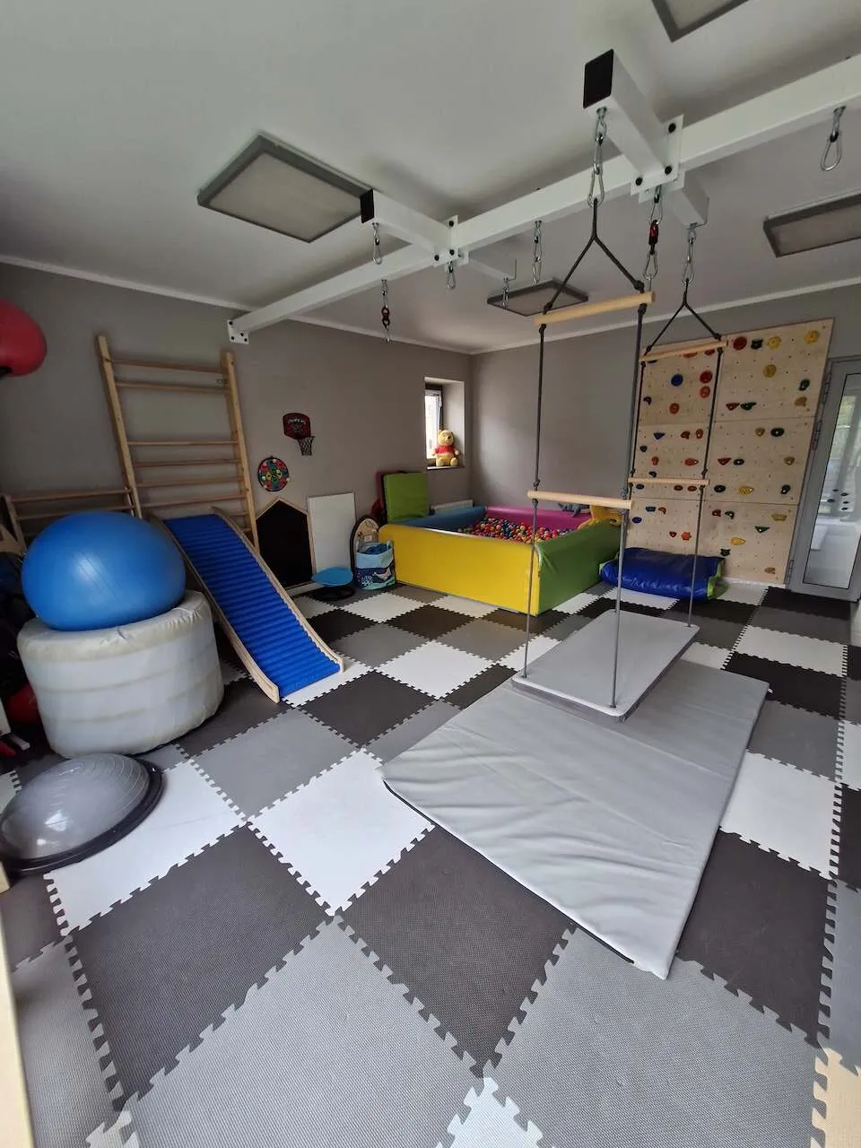 Sala integracji sensorycznej z huśtawką-platformą, równią, ścianką wspinaczkową i basenem z piłkami